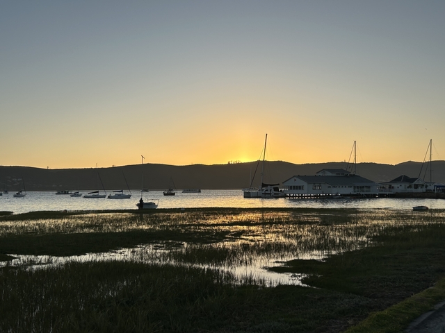 Sunset over a harbor with boats and calm waters.