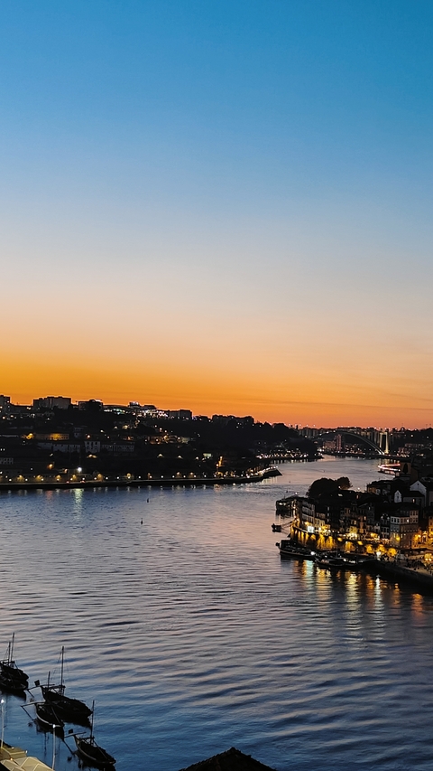       Sunset view over a city with lights reflecting in the river.
  