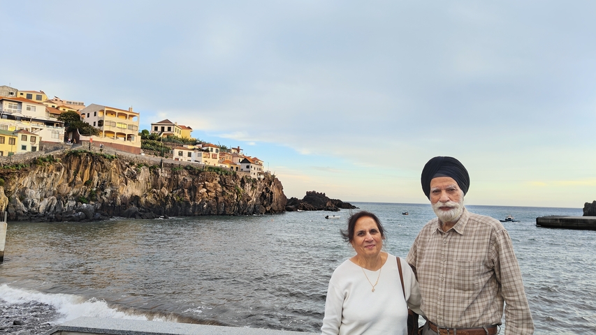       Two people posing by the seaside with a village on cliffs.
  