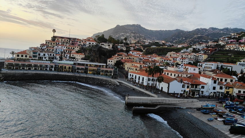       Coastal town with houses and mountain backdrop at sunset.
  