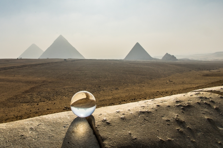       View of the Pyramids of Giza with a crystal globe on a stone ledge.
  