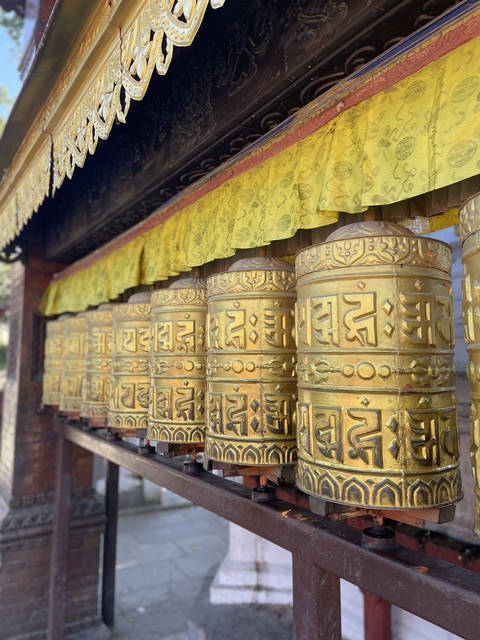       Row of ornate golden prayer wheels with inscriptions.
  