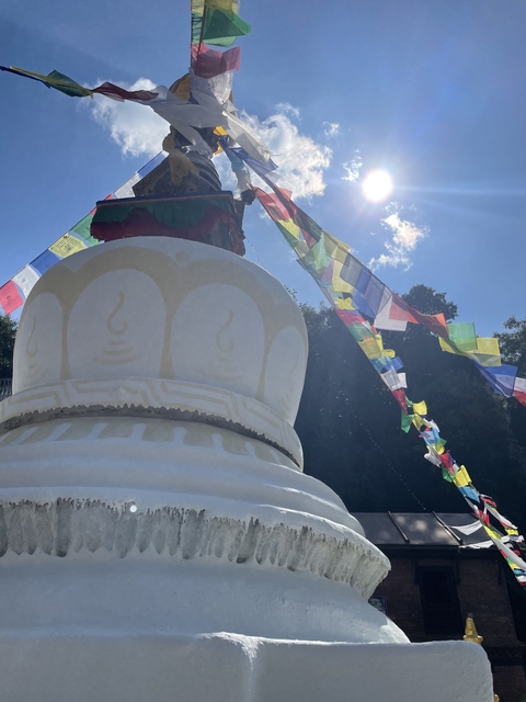       Close-up of a stupa with prayer flags and a bright sky.
  