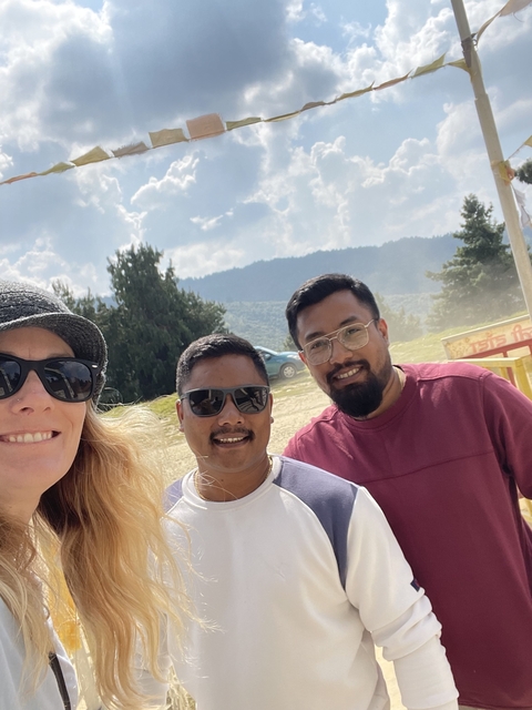       Three people posing outdoors with mountains in the background.
  