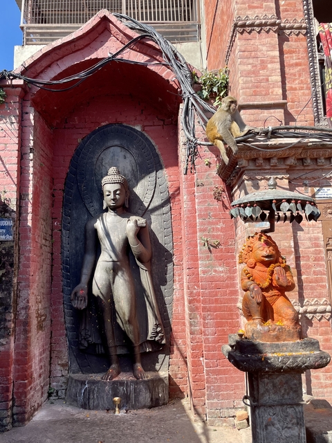       Buddha statue in a brick courtyard with a monkey nearby.
  