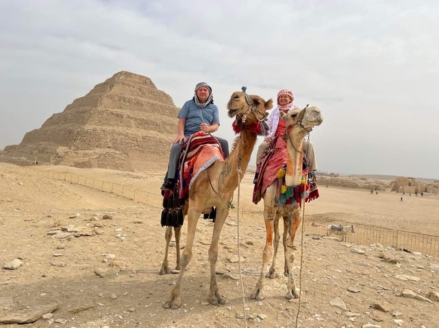 Two people riding camels near a pyramid.