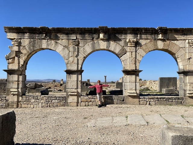 Person posing among ancient ruins with arches.