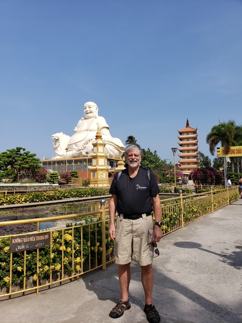 Statue of a seated Buddha with a pagoda in the background and a man standing in front.