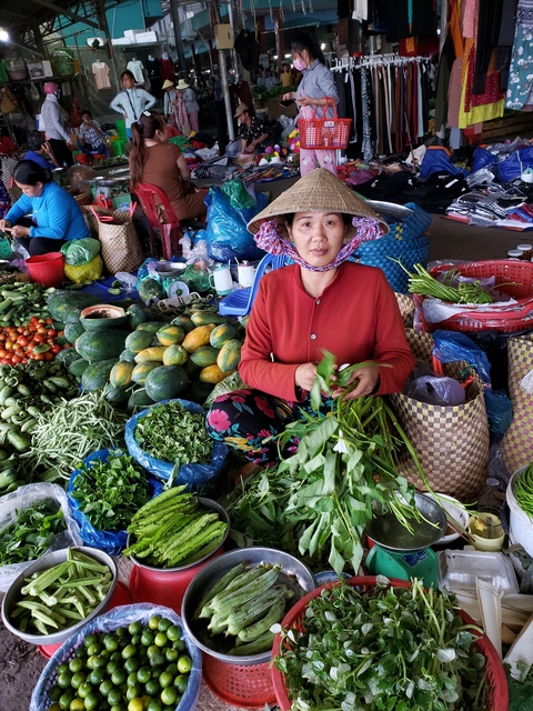 Woman sitting at a colorful market stall with vegetables and fruits.