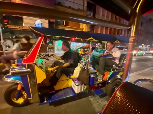 Blurry photo of people riding in a tuk-tuk on a city street at night.