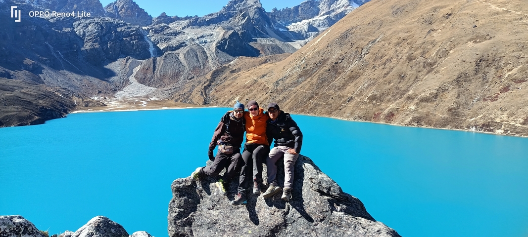       Three people posing on a rock above a turquoise lake with mountains around.
  
