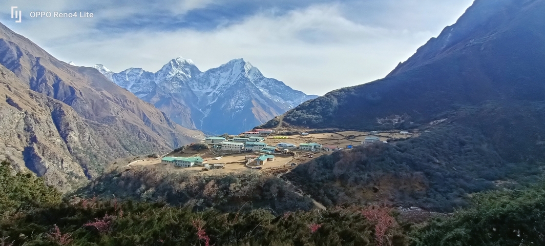       Person standing in front of a mountain village with snowy peaks in the background.
  