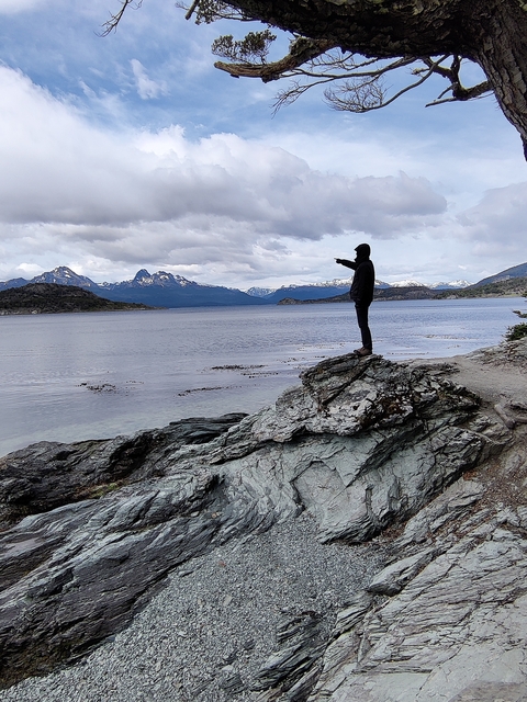 Person standing on a rocky shore pointing across the lake.