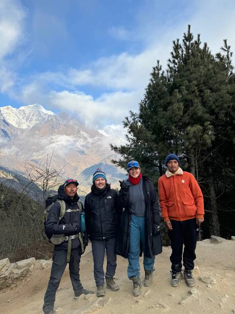       A group of people posing on a mountainous trail with snow in the background.
  