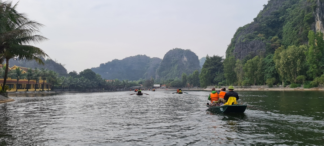 People rowing boats on a river surrounded by lush greenery and mountains.
