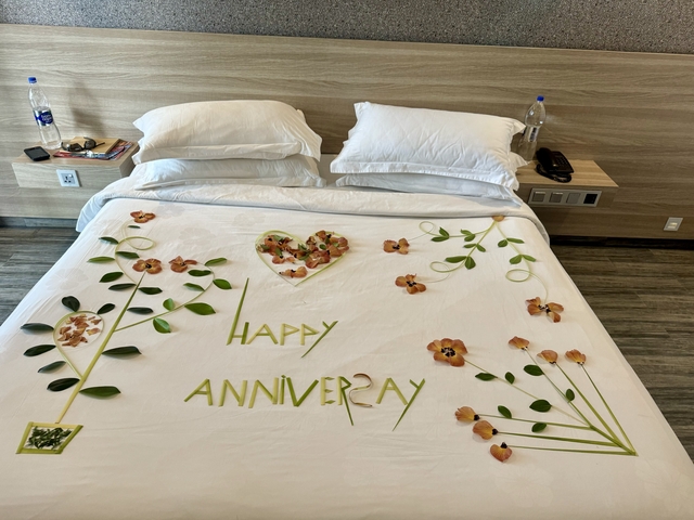       A bed with a decorative anniversary greeting made from leaves and flowers.
  