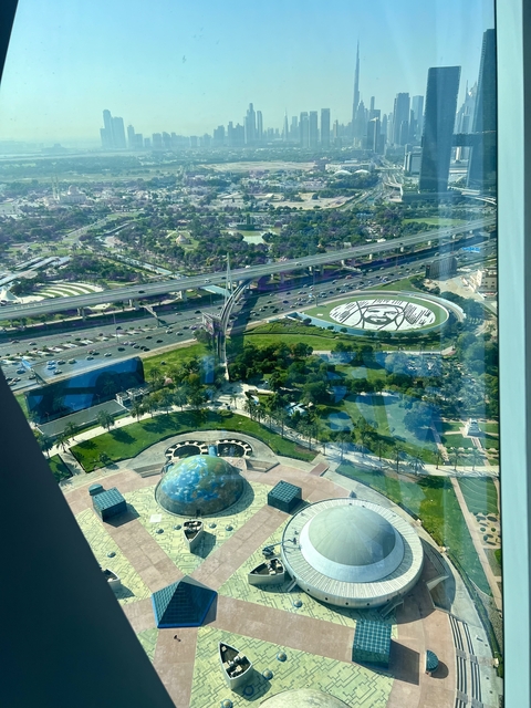       Elevated view of highways and a city park with a large face artwork.
  