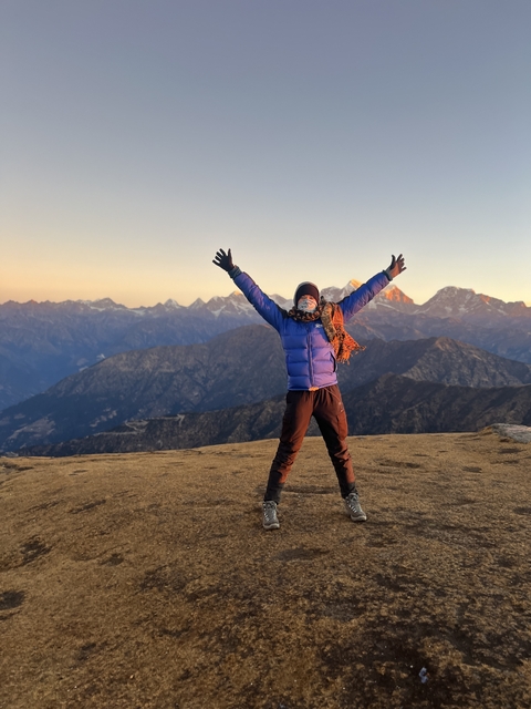 Person with arms raised on a mountain top at sunrise.