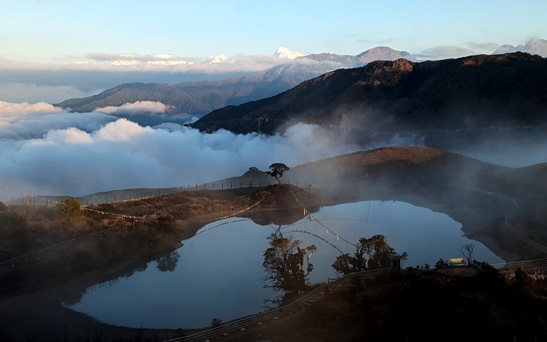 A scenic view of a lake surrounded by hills and clouds.