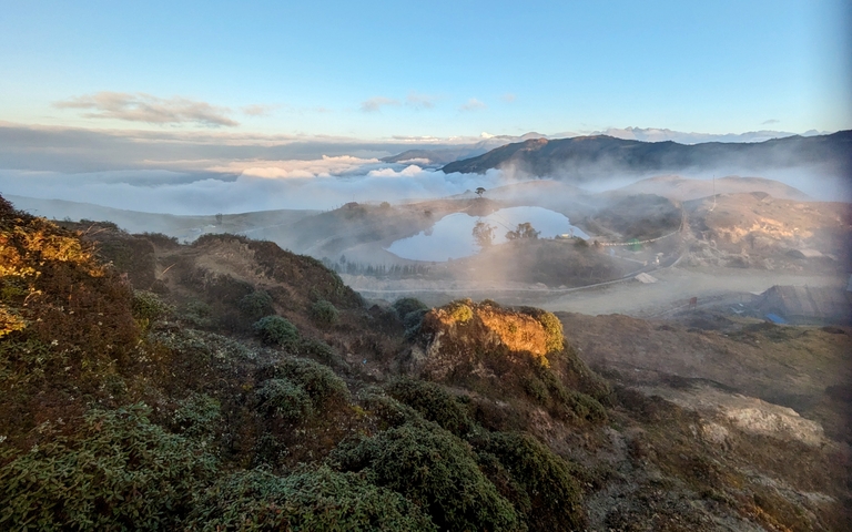       Panoramic view of a foggy landscape with hills and water.
  