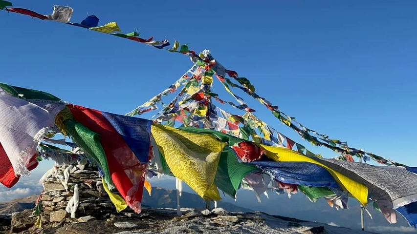       Colorful prayer flags on a mountain peak with a clear sky.
  