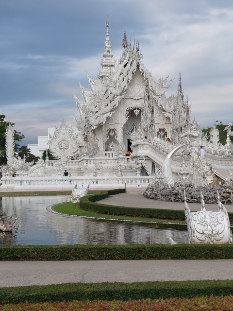 Ornate white temple with a garden and reflection pool.
