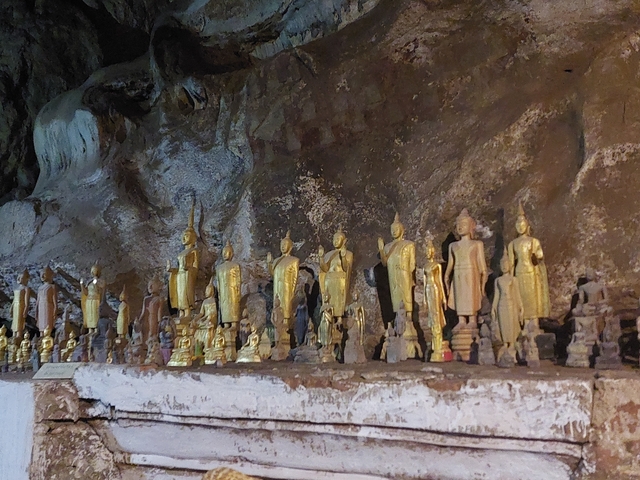 Row of golden Buddha statues in a cave setting.