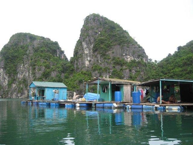 Floating houses on water with steep cliffs in the background.