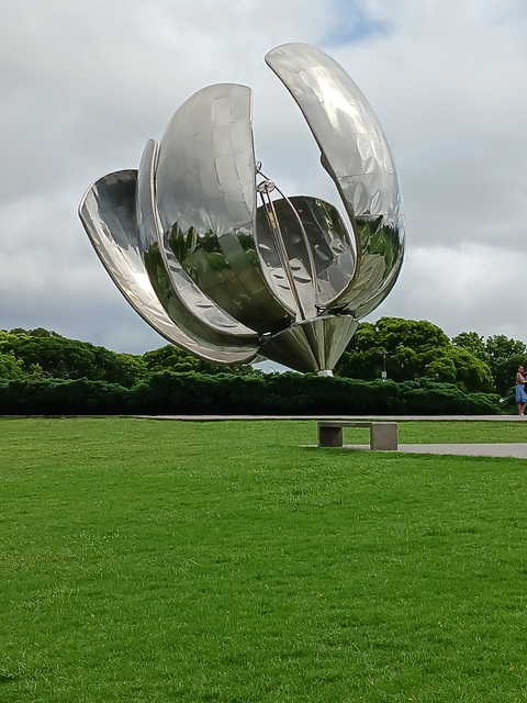 Close-up of a reflective metal sculpture in a park setting.