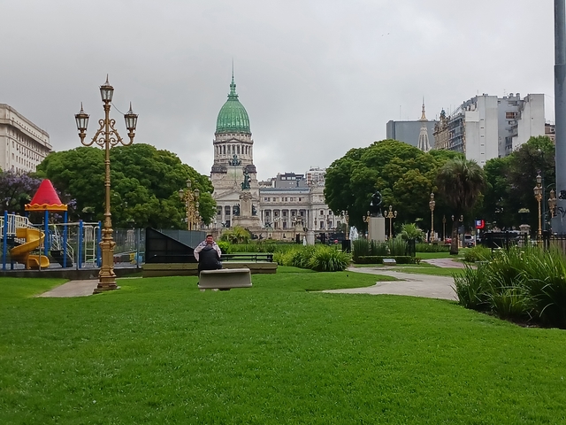 Park with a historical building in the background, featuring a person sitting.