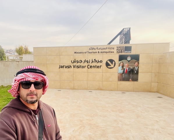       Individual posing in front of the Jarash Visitor Center sign in Jordan.
  