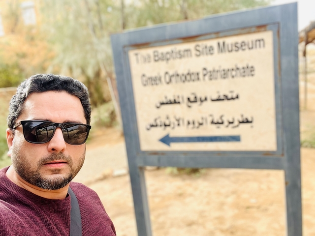 Person posing near a sign for the Baptism Site Museum.