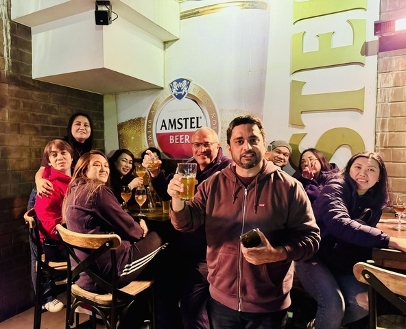      Group of people enjoying drinks at a bar with visible branding on the wall.
  