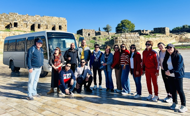       Group of tourists posing with a van and ancient ruins in the background.
  