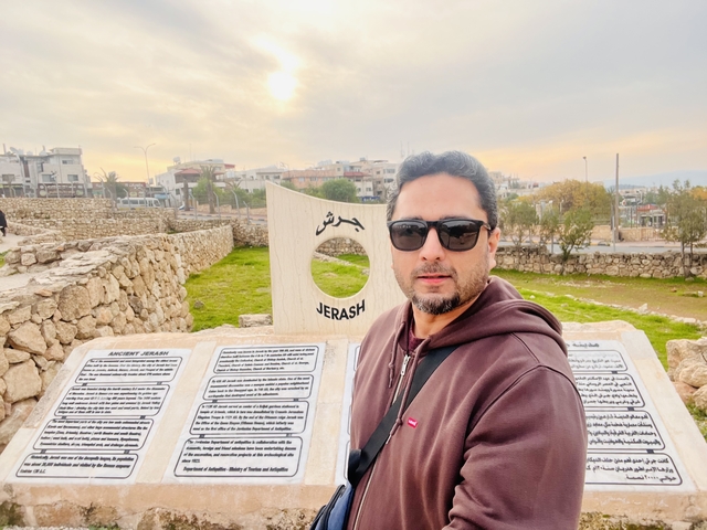       A person posing in front of a stone marker indicating Jerash.
  