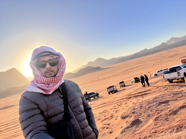 A person stands with jeeps driving on the desert in the background.