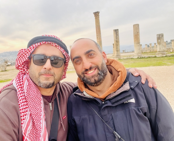       Two people smiling in front of ancient ruins with columns.
  