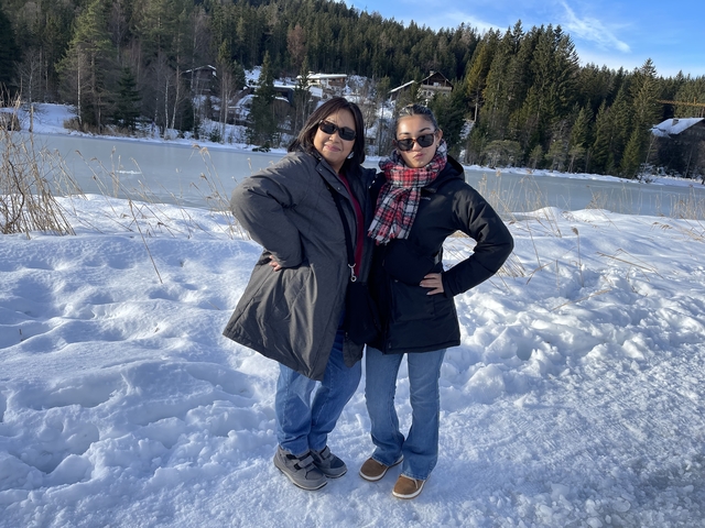 Two women posing by a snowy lake with trees in the background.