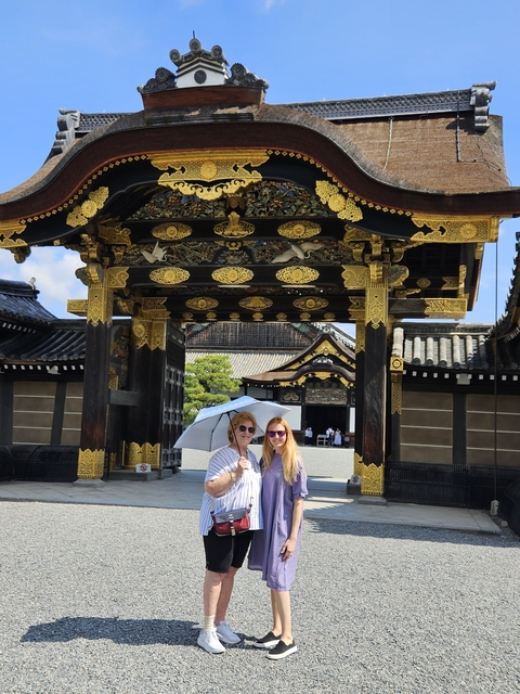       Two people standing under an ornate Japanese gate with an umbrella.
  