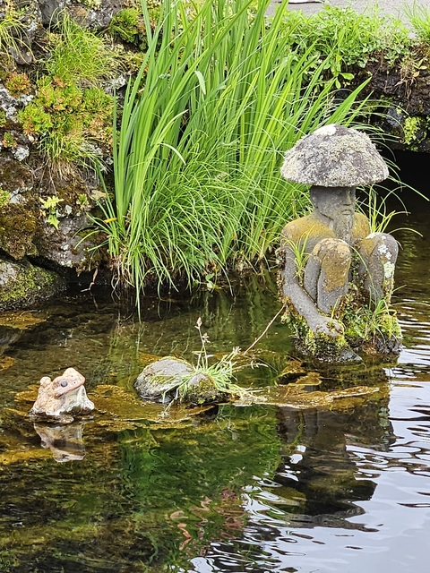       Stone statues in a garden pond with green vegetation.
  