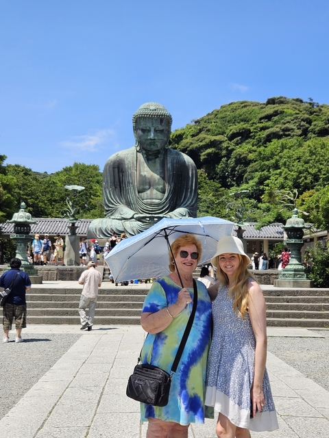       Two people posing in front of a large Buddha statue, under a sunny sky.
  