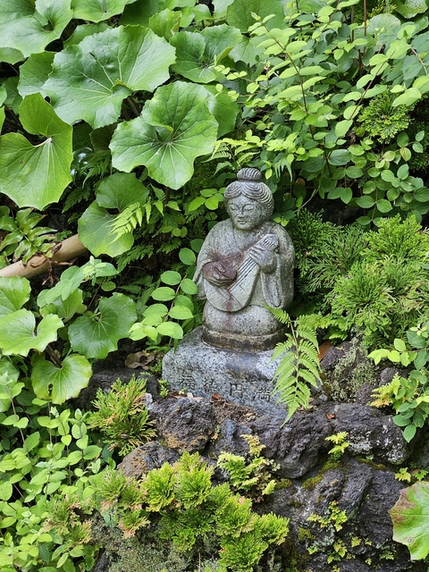       A stone statue of a musician in a lush garden.
  