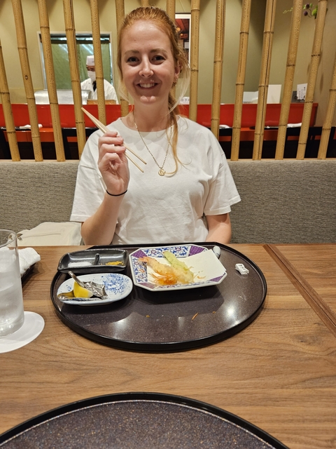       A woman dining in a restaurant with chopsticks.
  