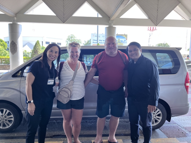 Four people posing in front of a van at an airport drop-off.