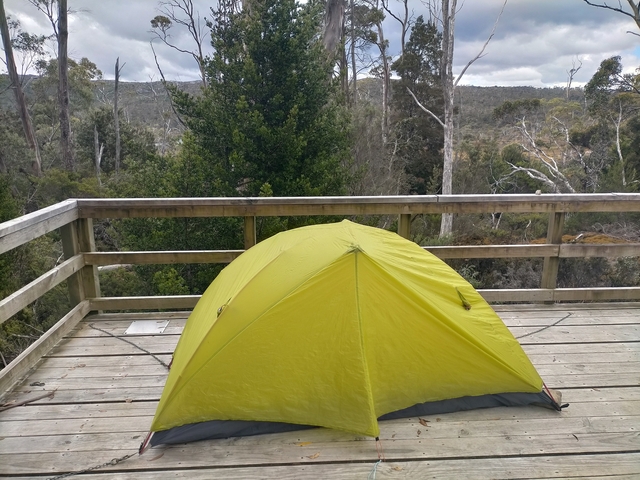A yellow tent on a wooden deck overlooking a forest.