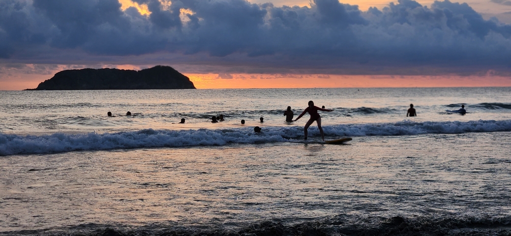 Sunset over the ocean with people swimming.