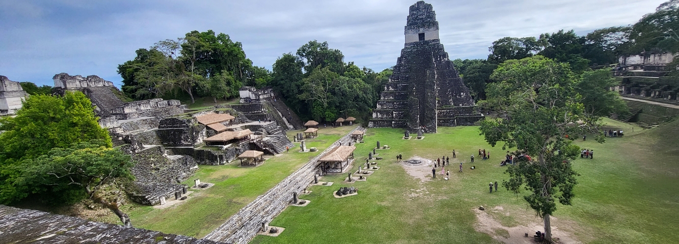       Ancient Mayan ruins with a large pyramid and people walking around.
  
