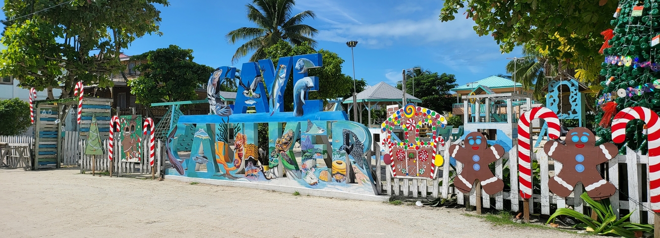 Colorful sign reading 'Caye Caulker' with decorations and trees in the background.