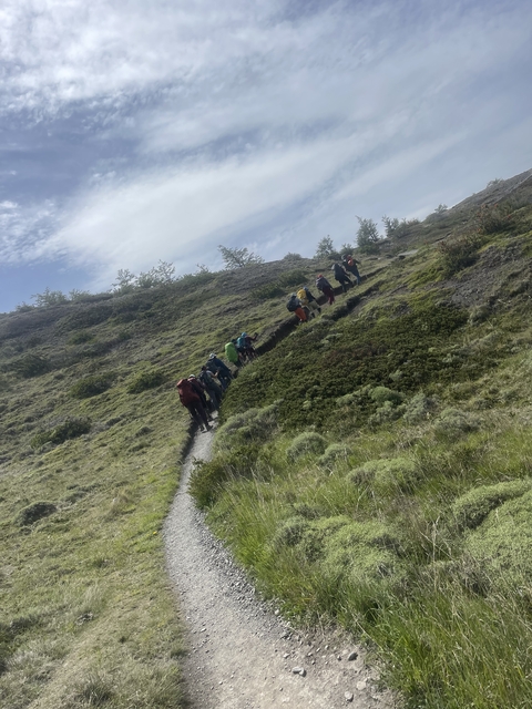       People hiking on a hilly path with greenery around.
  