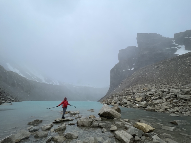       Person standing near a glacial lake surrounded by mist.
  